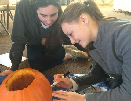 Staples students Annie Haroun ’16 and Eliza Donovan ’16 start the pumpkin carving process by outlining their idea.