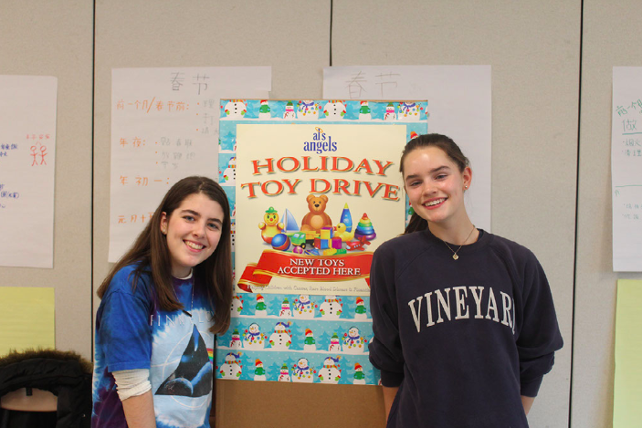 Merin McCallum 21 and Savannah Schaefer 21 pose next to the Holiday Toy Drive donation box