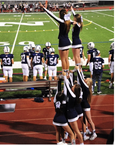 Staples cheerleaders wearing gameday uniforms on the football field sideline during a Friday night game at Norwalk High School. 
