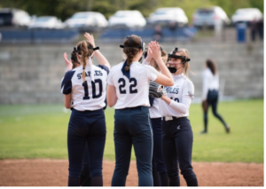The Staples Varsity softball team high-fives last year before COVID-19 began. This year, social distancing and mask wearing will be enforced so on field play will be very different. 