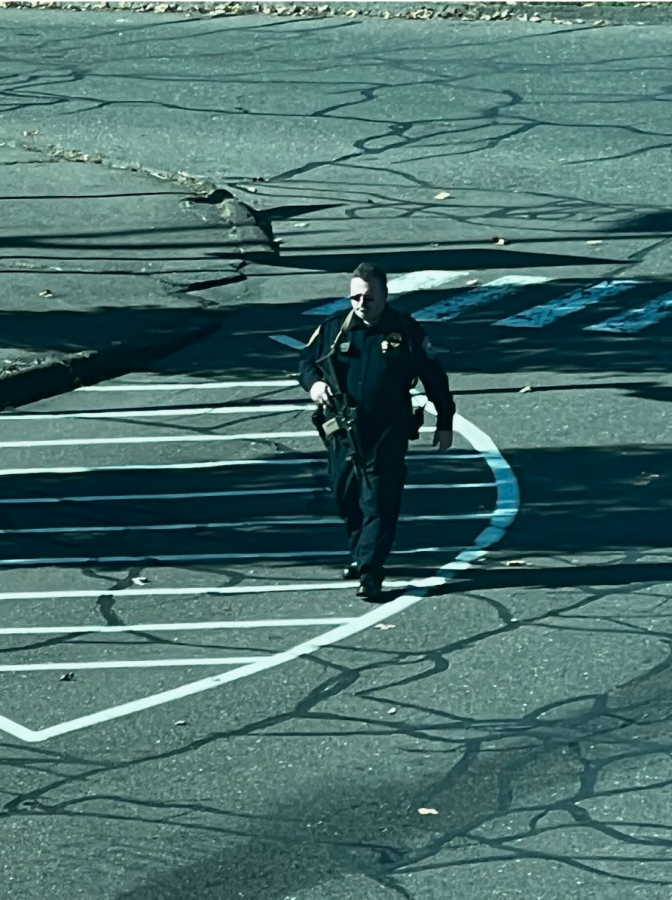 An armed Westport police officer walks towards Staples to evaluate the swatting threat. 
